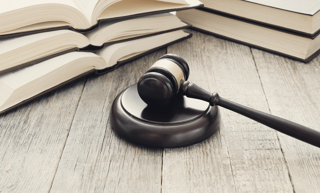 acessível. Imagem de um martelo da justiça em cima de uma mesa e ao lado de alguns livros abertos. 