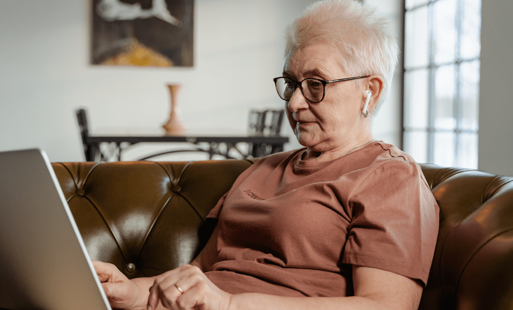WCAG. na imagem, temos uma senhora sentada no sofá mexendo no notebook, que está em seu colo