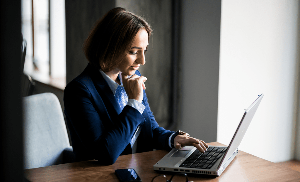 ESG. Imagem de uma mulher vestida de roupa social em uma sala de reunião mexendo no notebook e com uma das mãos segurando o queixo.