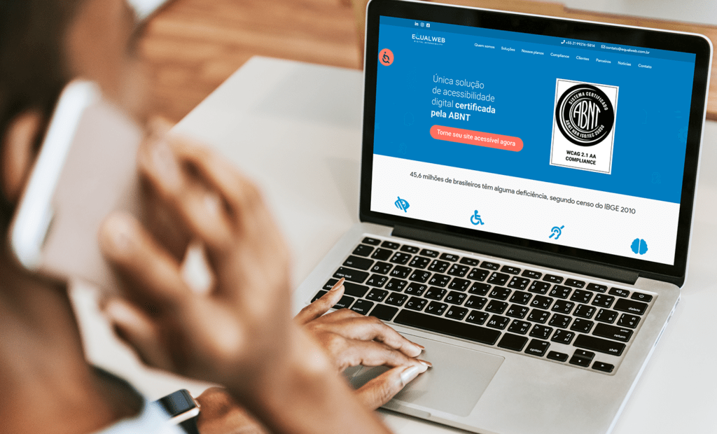 deficiência. Imagem de uma mulher negra usando o telefone e o notebook. O Notebook está com o site da EqualWeb aberto na página inicial.