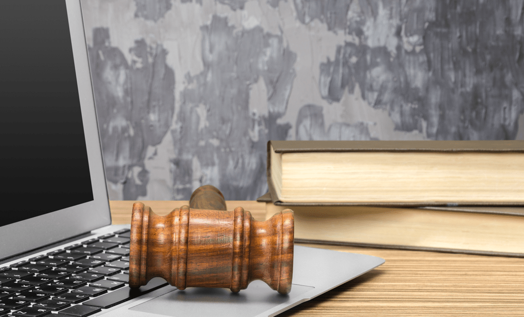 entretenimento. Imagem de uma mesa com um notebook e alguns livros. Em cima do notebook tem um martelo de madeira.