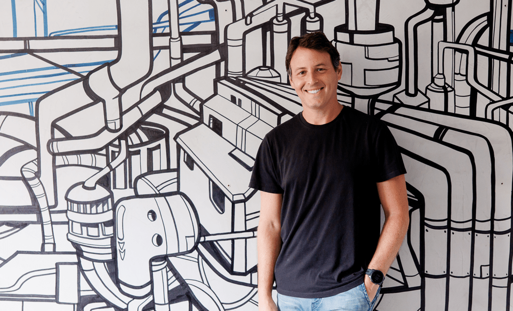 CVC Corp. Imagem do  Head de Impacto e Influência da EqualWeb, Jaques Haber. Um homem branco de cabelos pretos, vestindo uma blusa preta e calça jeans. Ele está encostado em uma parede com alguns desenhos. 