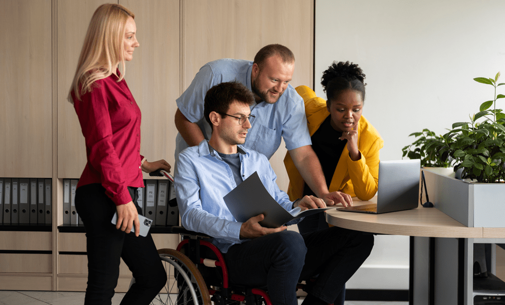 Campanhas. Imagem de um grupo de pessoas olhando para o computador. Na imagem podemos observar uma mulher loira de cabelos longos, uma homem branco de cabelos curtos, uma mulher negra e um homem branco cadeirante.
