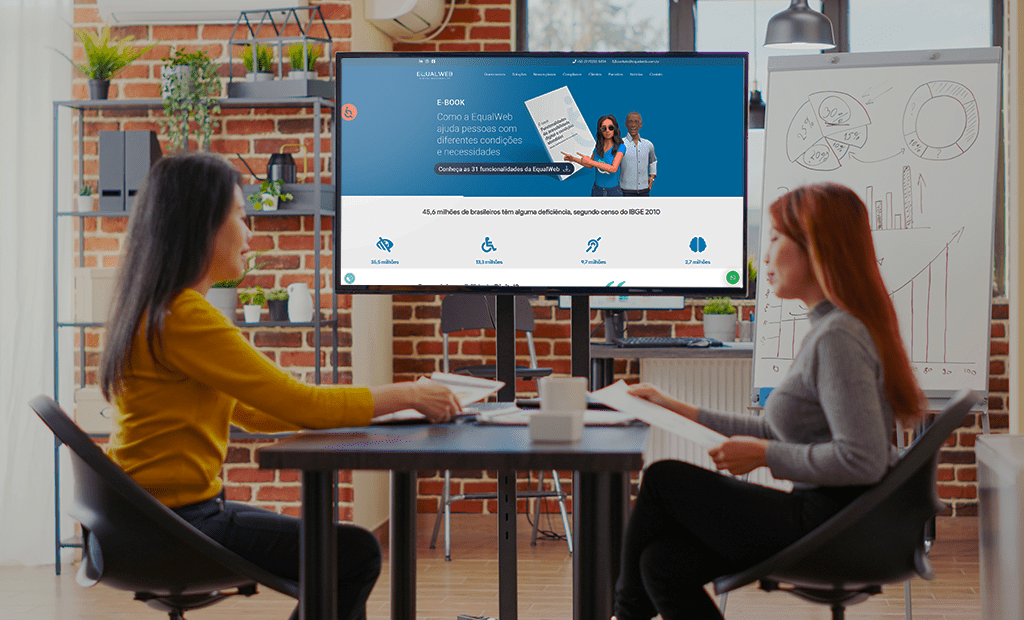 acessinilidade digital. Imagem de duas mulheres orientais em uma sala de reunião conversando e ao fundo uma tela mostrando o sita da EqualWeb aberto na home. 
