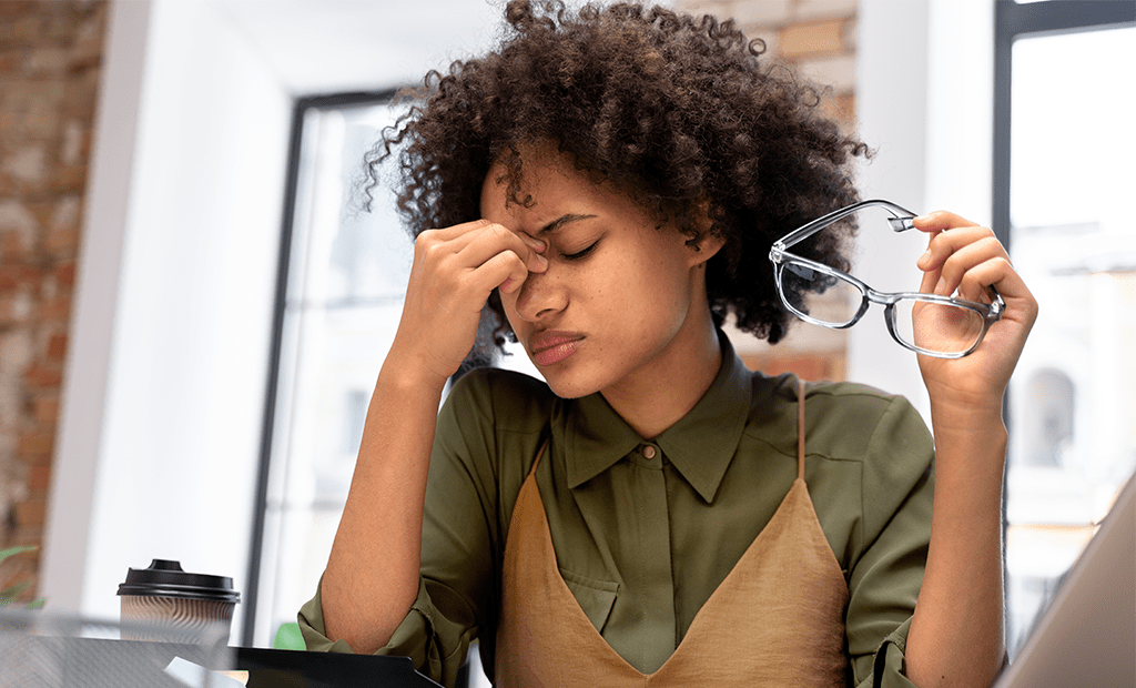 Acessibilidade financeira. Imagem de uma mulher negra , cabelos preto segurando um óculos com uma das mãos e a outra mão no rosto com a feição de preocupada.