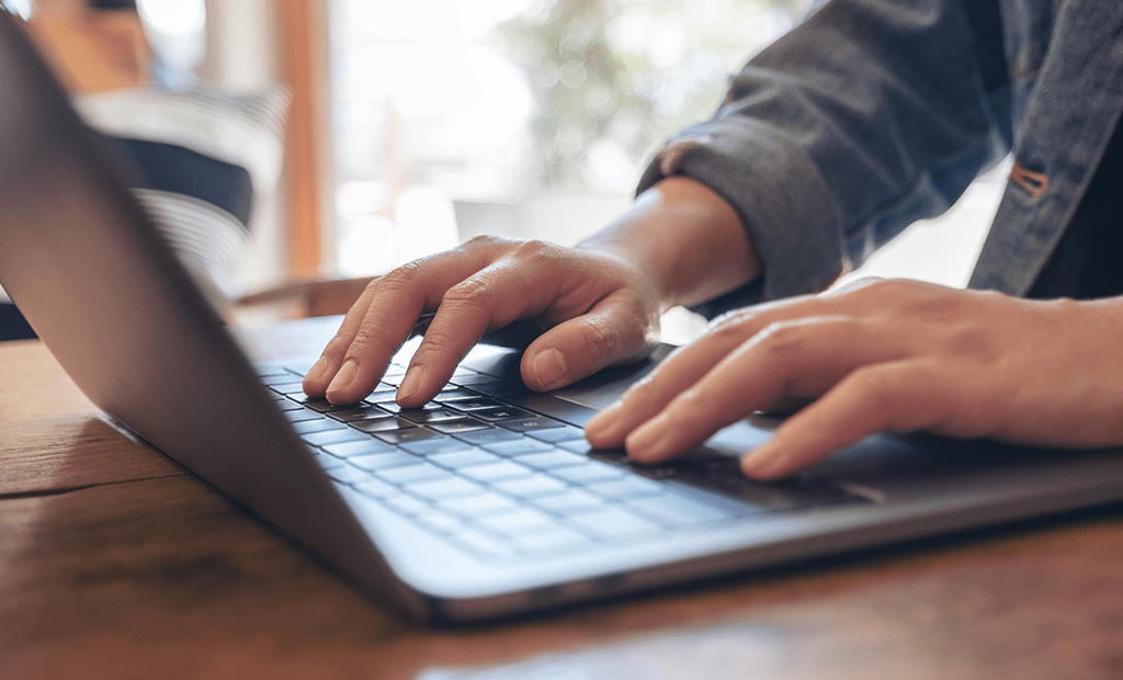 Descrições. Imagem de uma mão masculina mexendo em um notebook.