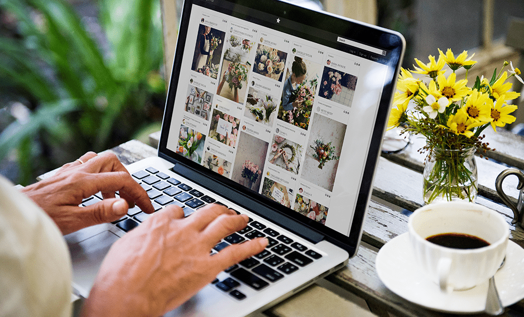 Descrições. Imagem de uma mão feminia mexendo em um notebook e ao lado uma xícara de café. 