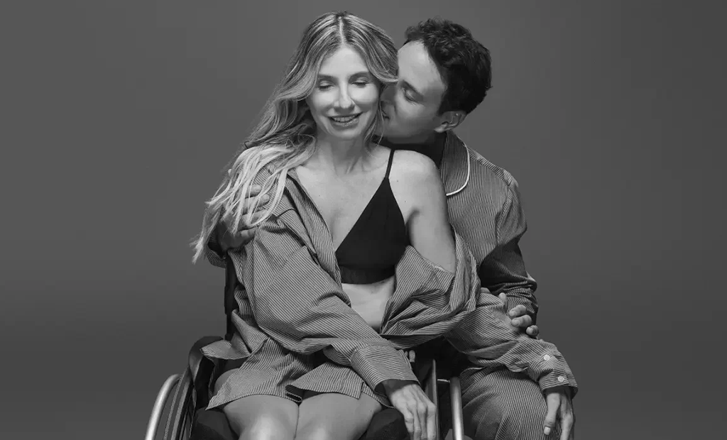 Reserva. Casal de pessoas brancas, formado por um homem e uma mulher. Ela com cabelos longos, soltos e claros, ele com cabelos curtos e castanhos. Ele abraça ela por trás e ela segura as pernas dele. 