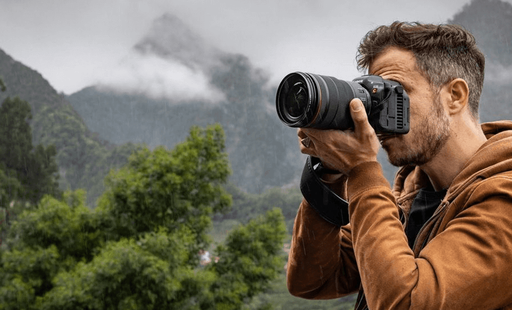 Descrições. Fotógrafo usando a Câmera digital Canon EOS R5, na cor preta, para capturar imagens e vídeos de uma bela paisagem em 8K.