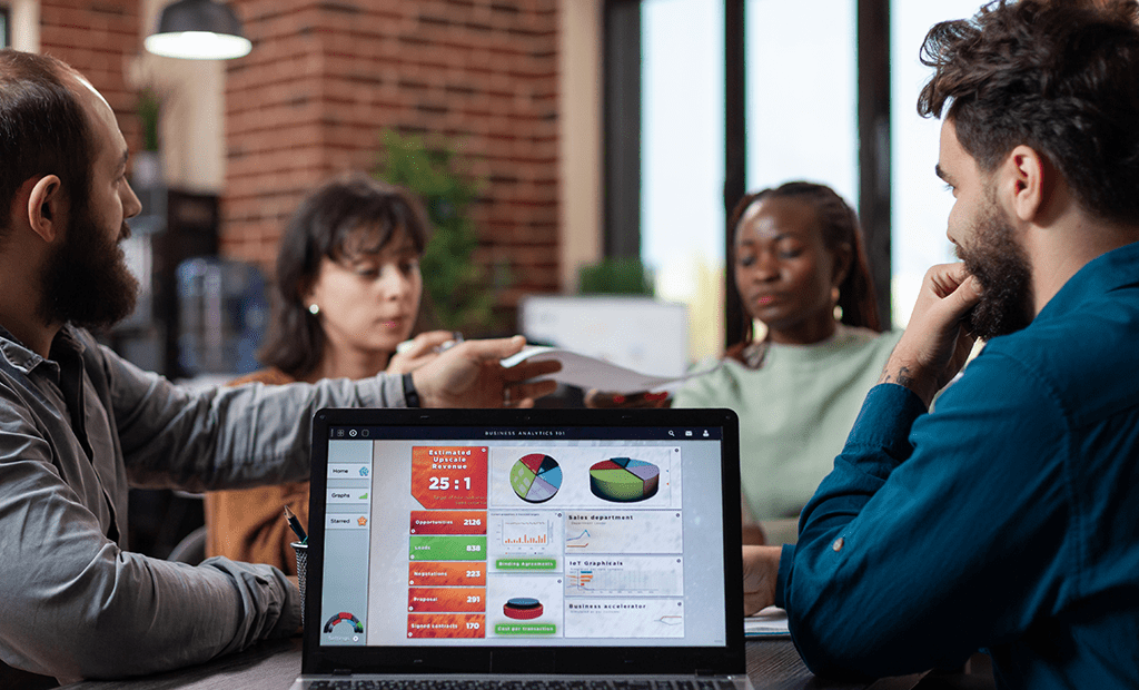 Descrições. Quatro pessoas de diferentes etnias em uma reunião de negócios, discutindo gráficos na tela de um laptop.