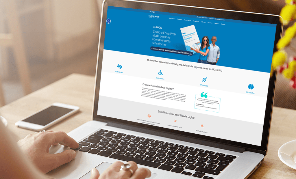 ROI. Laptop exibindo a página inicial do site da EqualWeb brasil. Há um smartphone colocado próximo ao laptop e um pequeno arranjo de flores amarelas ao lado.
