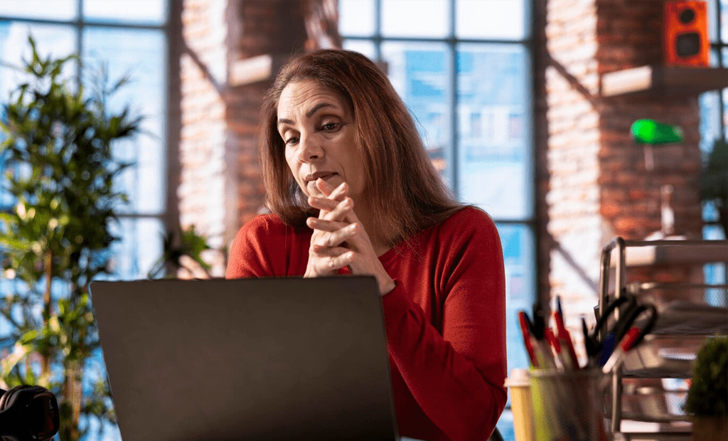 WCAG. Mulher de suéter vermelho concentrada no notebook em um ambiente de escritório.