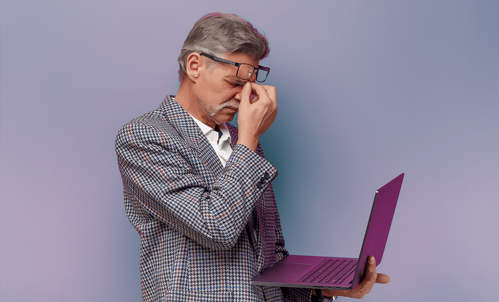 wcag. Homem grisalho com notebokk na mão, apertando o nariz com expressão de cansaço