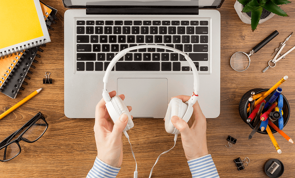 Autismo. Pessoa segurando fones de ouvido brancos em frente a notebook, materiais de escritório sobre a mesa.