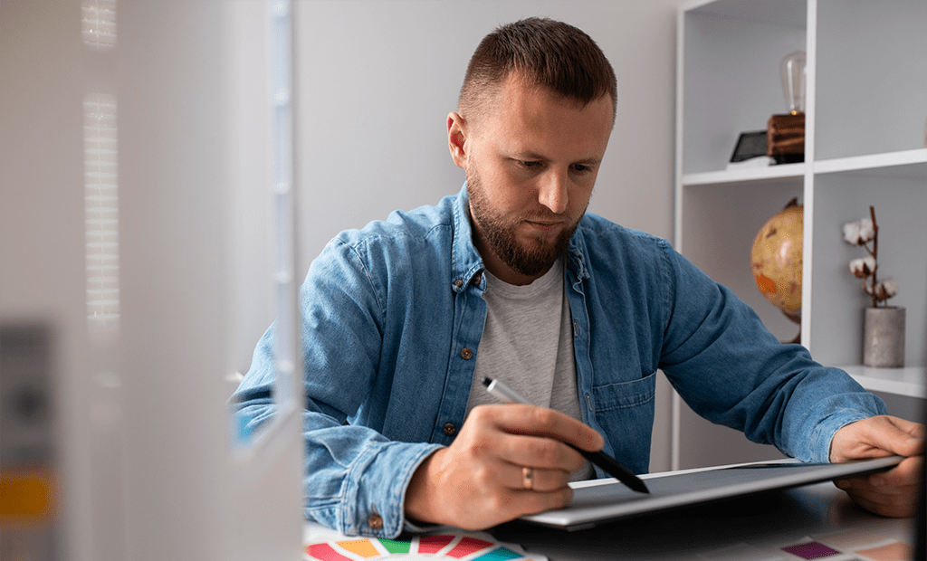 Autismo. Homem trabalhando concentrado com caneta digital e um tablet, em ambiente de escritório.