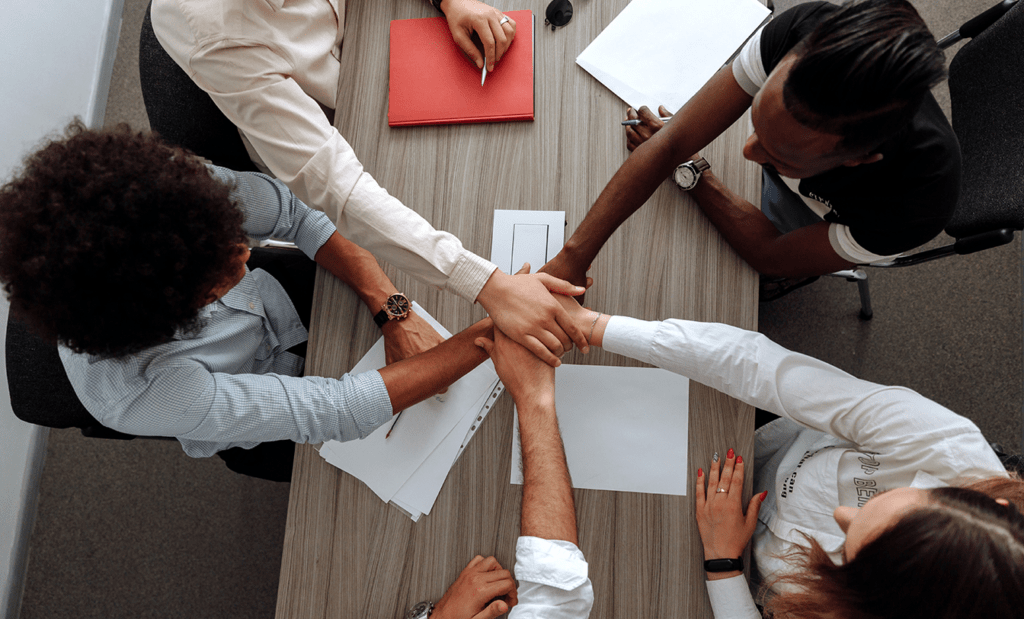 deficiência. Imagem de um grupo de pessoas de mãos dadas por cima de uma mesa em uma sala de reunião.