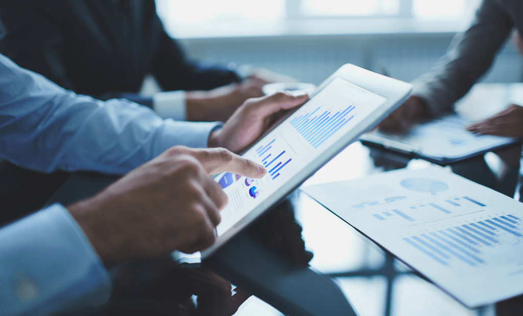 ESG. Na imagem podemos observar três homens em uma sala de reunião, todos vestindo roupas sociais. Um segura um tablet mostrando alguns dados na tela e os outros dois estão fazendo anotações.