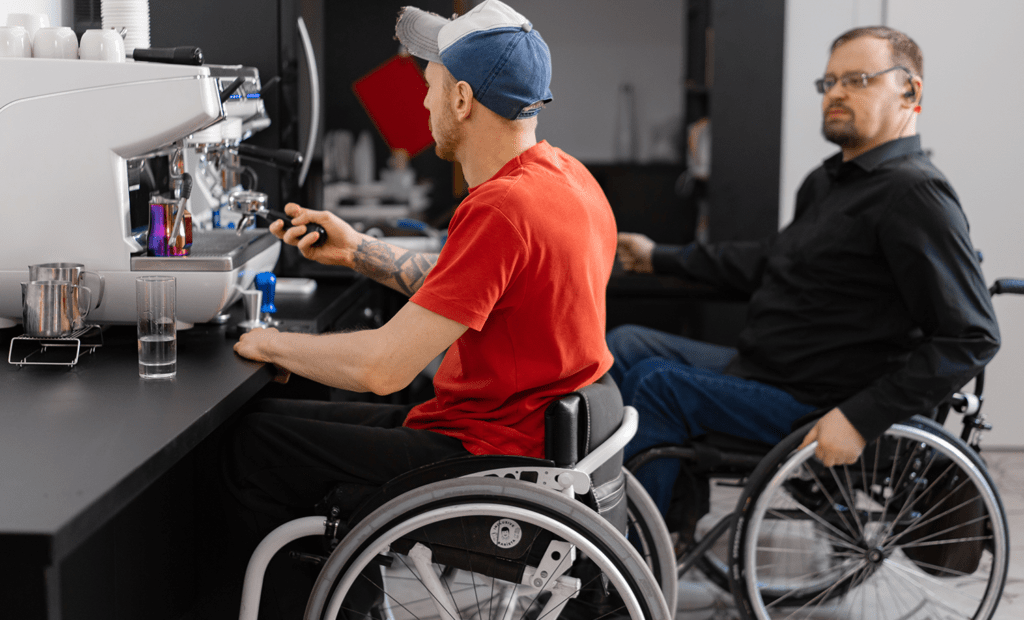 estudo. Na imagem podemos observar dois homens cadeirantes, trabalhando em um laboratório de análise s. Um homem veste camisa vermelha e boné azul e o outro veste um casaco petro e usa óculos.