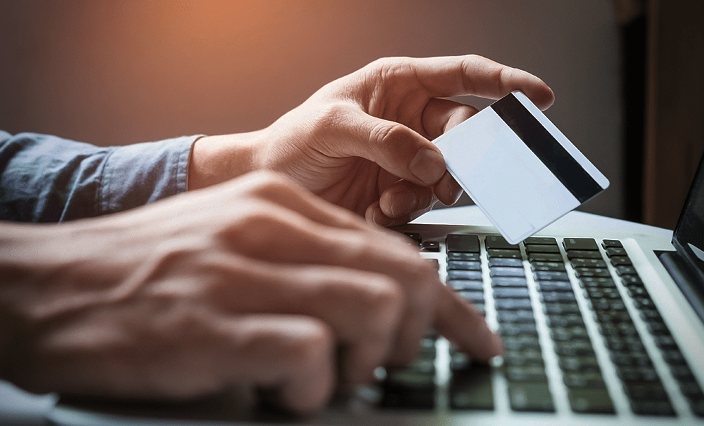 Acessibilidade Financeira. Imagem de uma mão masculina digitando em um notebook e na outra mão segurando um cartão de crédito.