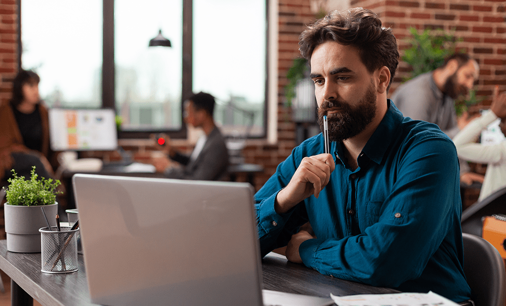 Dúvidas. Imagem de um homem branco, barba e cabelos grandes, olhanda para uma tela de computador.