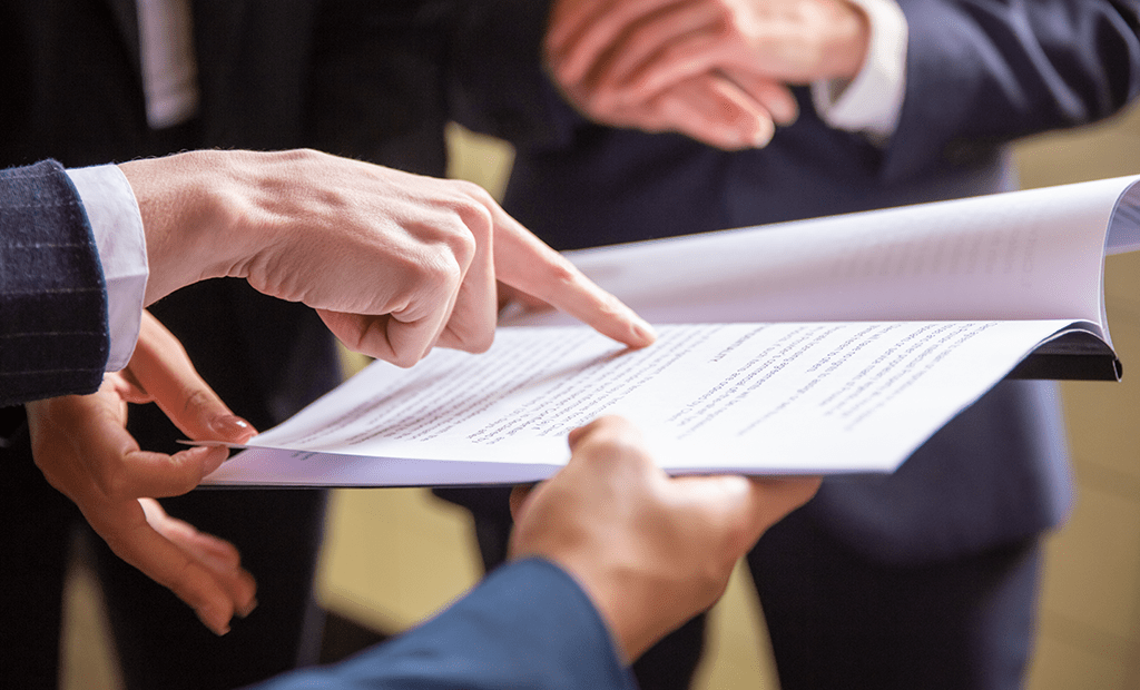 ABNT. Grupou de pessoas vestindo trajes formais analisando um documento. Uma mão aponta para um trecho do papel.