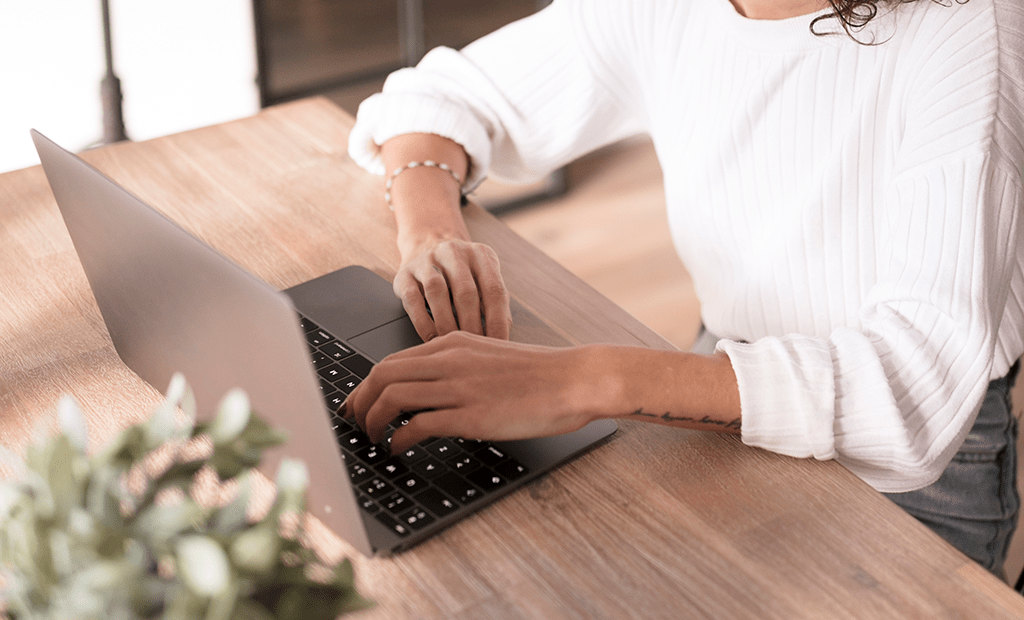 Termômetro. Pessoa usando um laptop sobre uma mesa de madeira, com uma planta desfocada em primeiro plano.